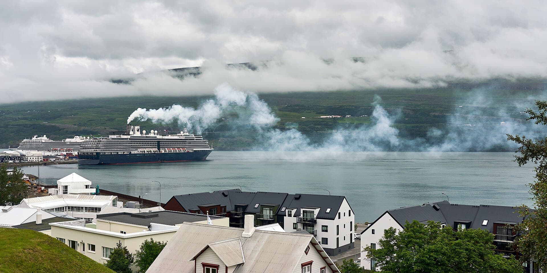 A cruise ship at the pier in Akureyri, Iceland, with fjord mountains behind.