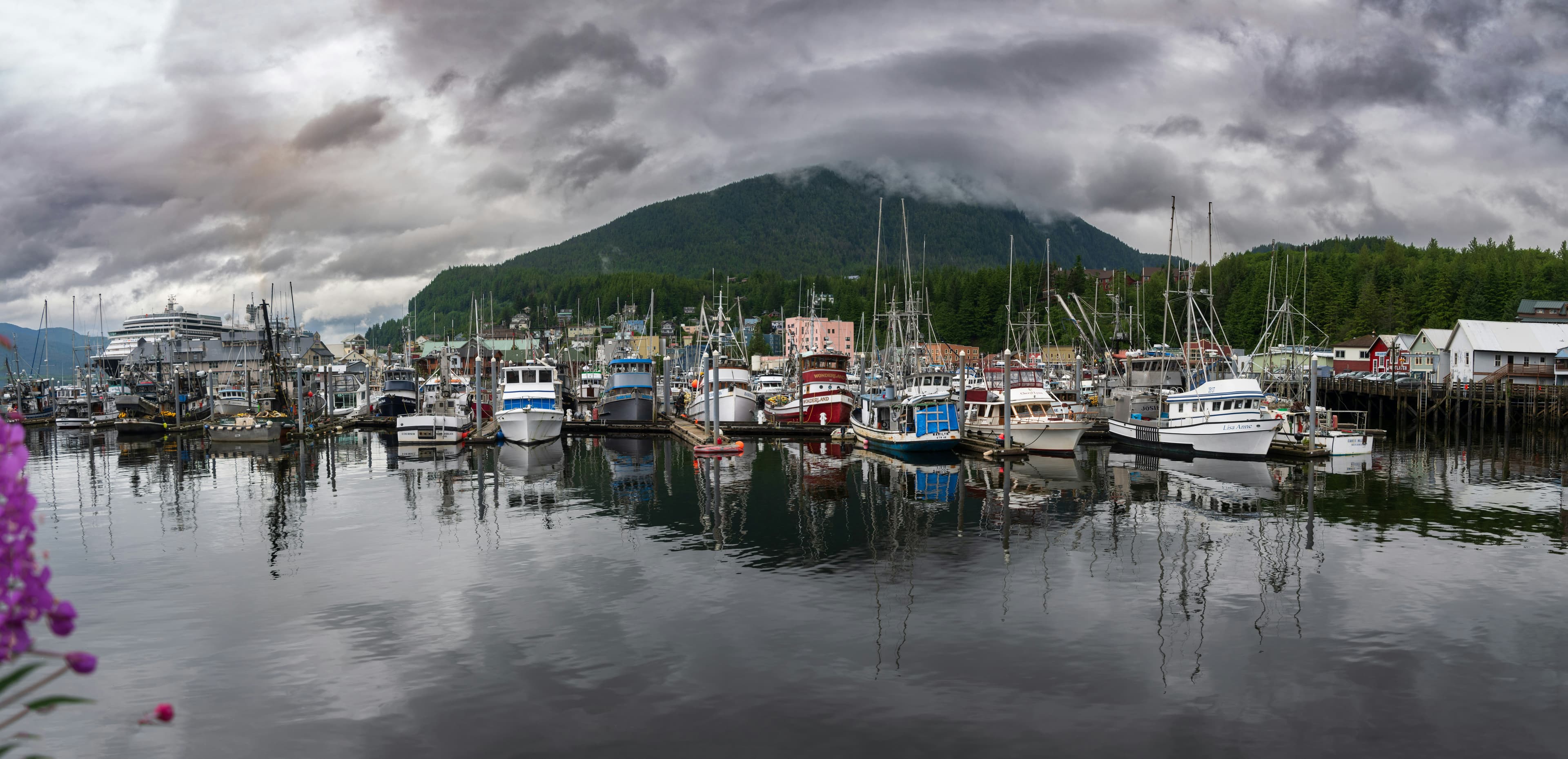 Ketchikan harbor with boats, misty mountains, and a cruise ship in the distance.
